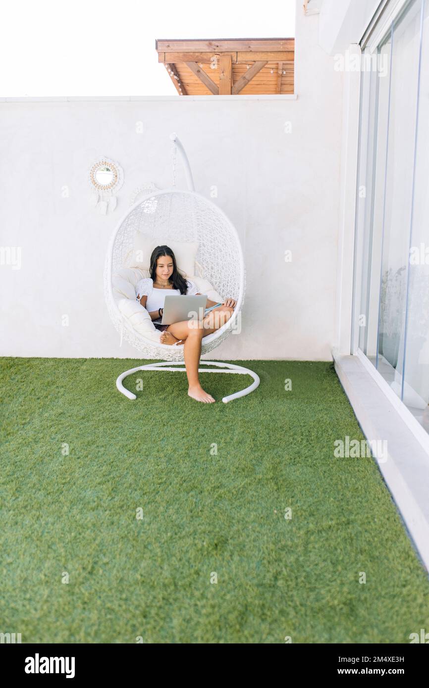 Ragazza che usa un computer portatile seduto su una sedia sospesa sul retro Foto Stock