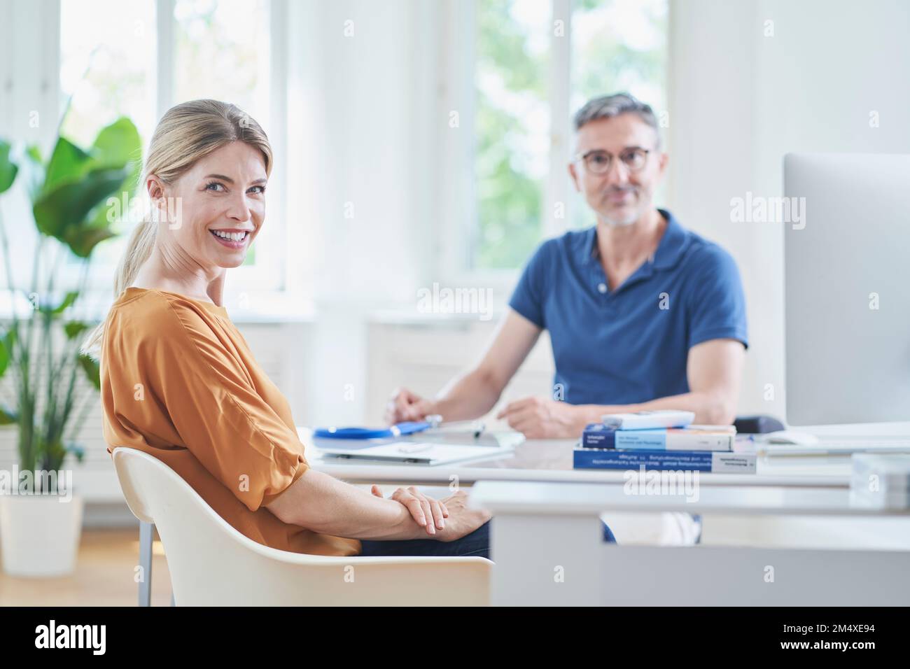 Donna felice seduta su sedia con medico in background alla pratica medica Foto Stock