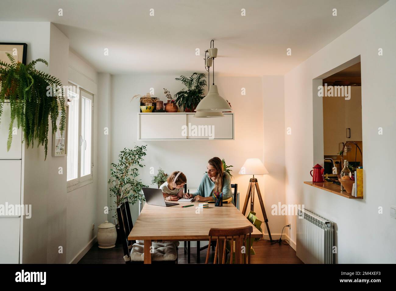 Madre che spiega la figlia seduta con il portatile al tavolo a casa Foto Stock