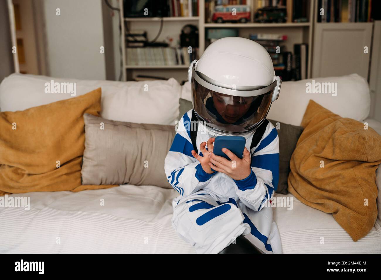 Ragazza che indossa il costume da spazio usando lo smartphone sul divano nel soggiorno Foto Stock