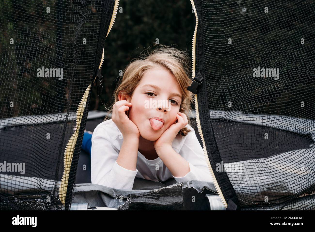 Ragazza che si stacca la lingua sdraiata sul trampolino in giardino Foto Stock