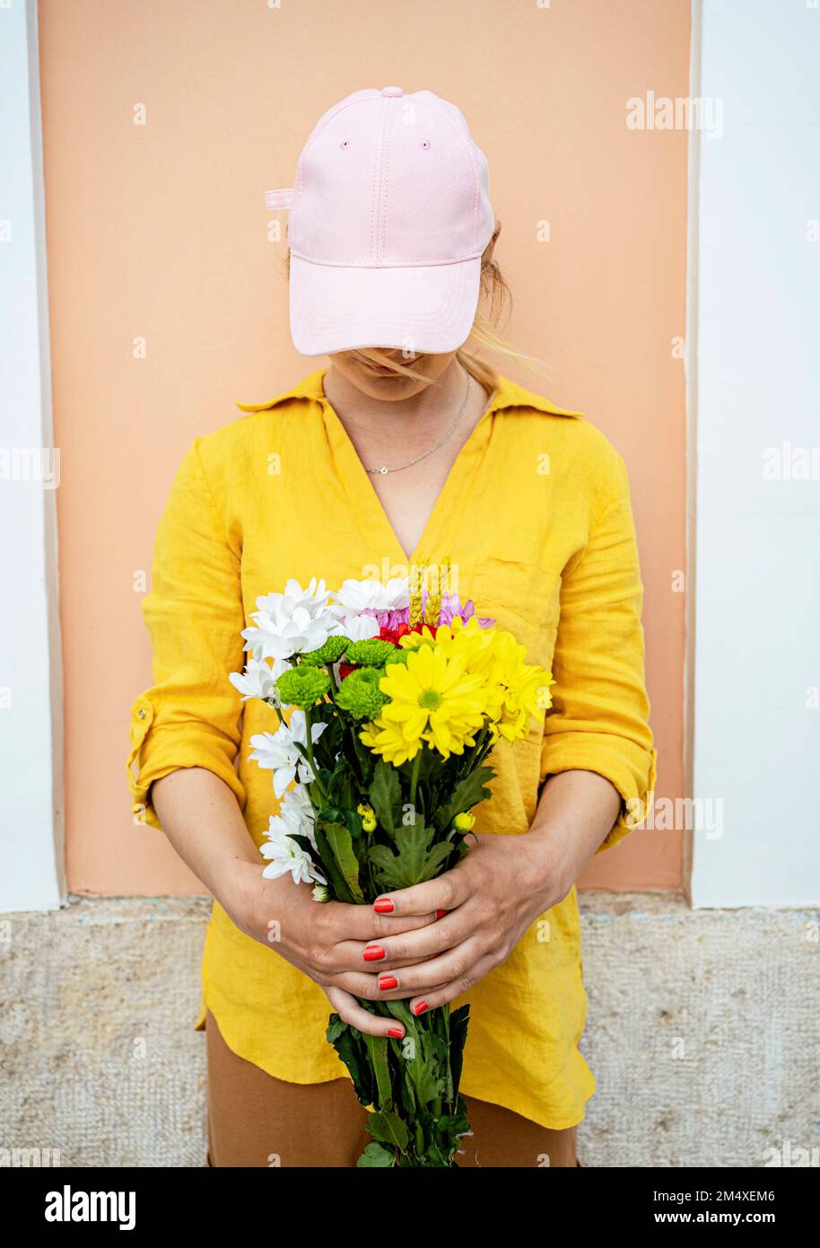 Giovane donna che indossa il cappuccio in piedi con fiori davanti al muro Foto Stock