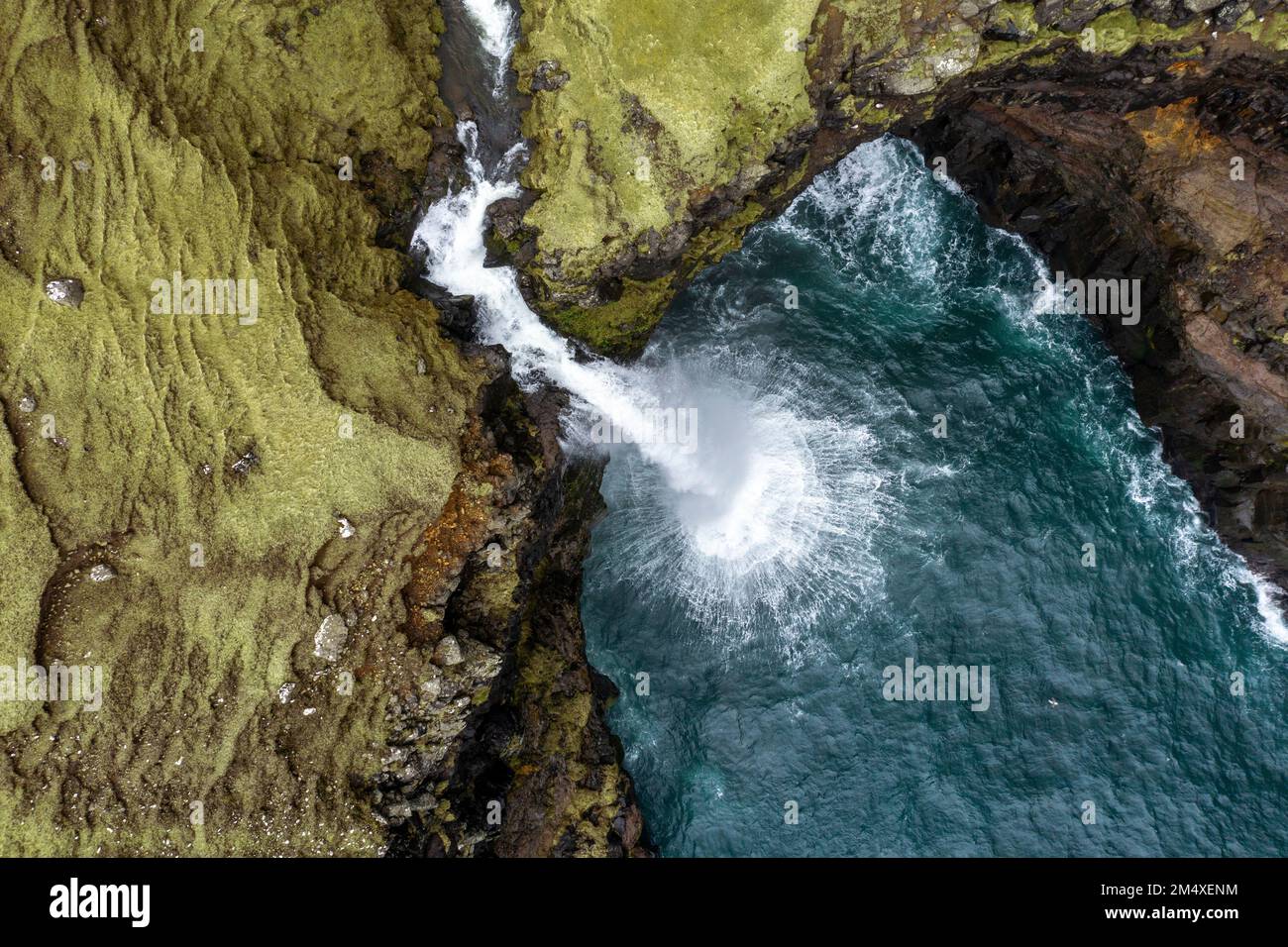 Cascata di Mulafossur tra montagne rocciose Foto Stock