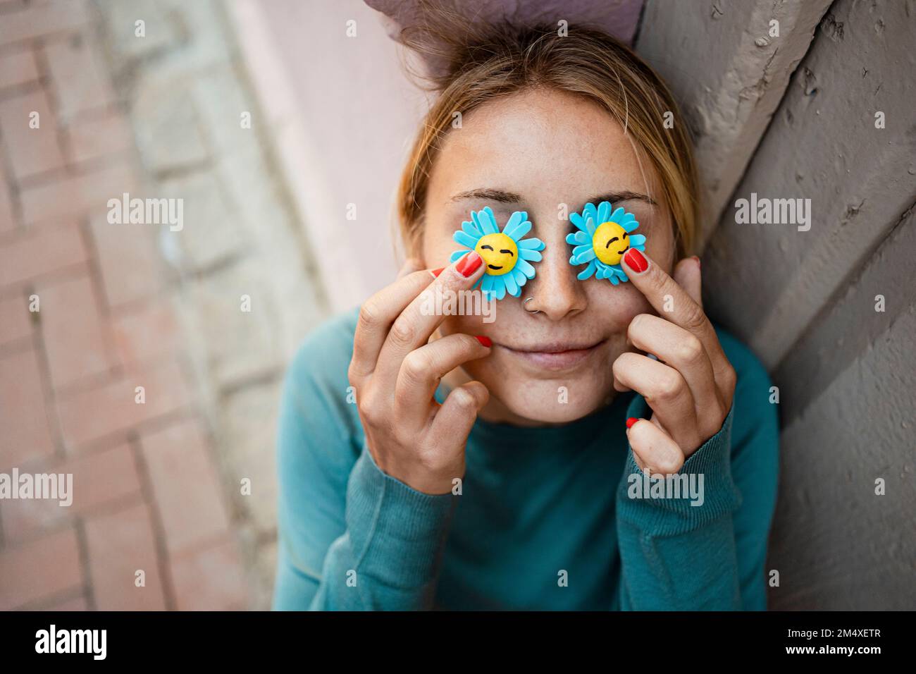 Giovane donna sorridente che tiene il fiore artificiale sopra gli occhi Foto Stock