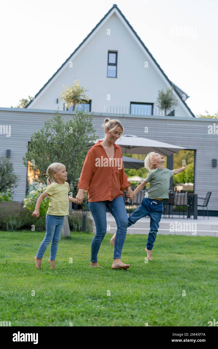 Madre giocosa che tiene le mani dei bambini che giocano in giardino Foto Stock