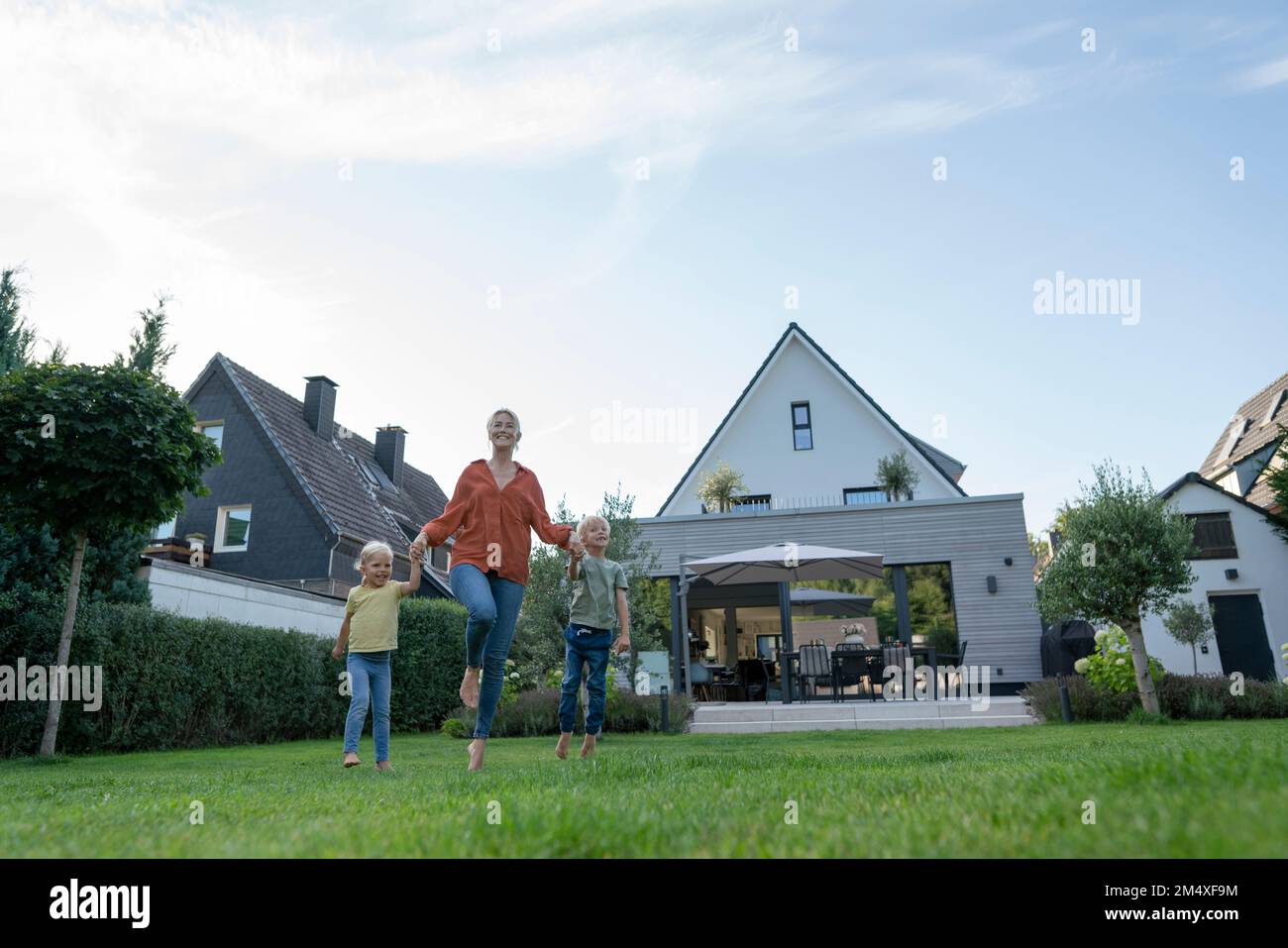Donna allegra che tiene le mani dei bambini godendosi in giardino Foto Stock