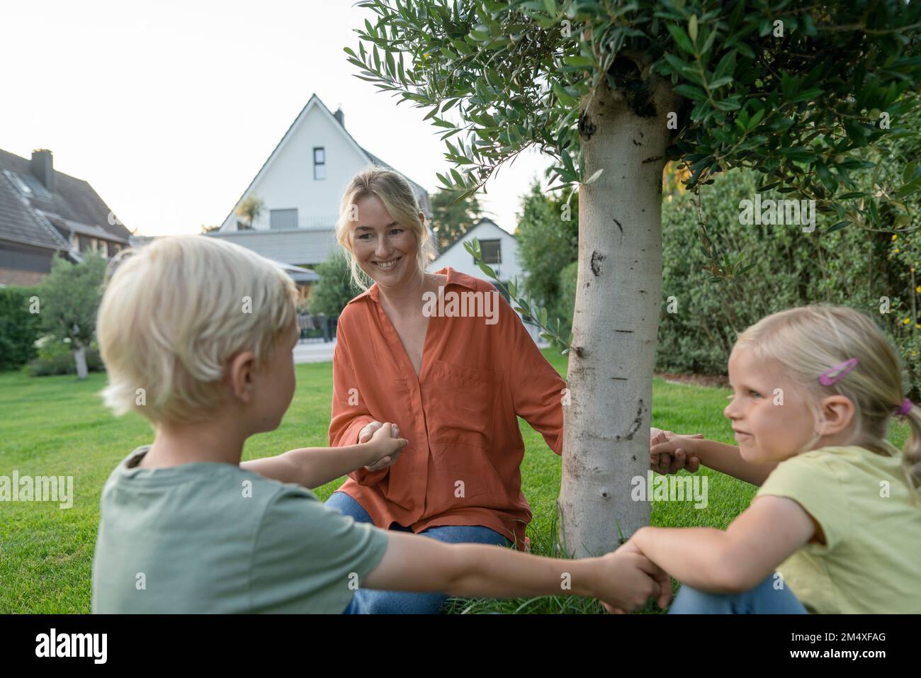 Madre sorridente che tiene le mani dei bambini in giardino Foto Stock