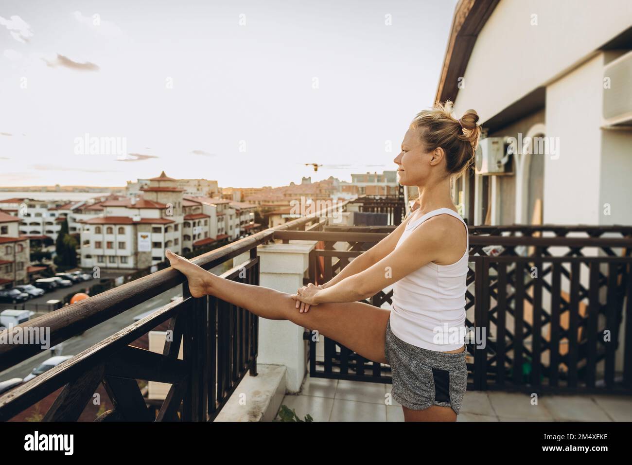 Donna che fa esercizio stretching sulla terrazza sul tetto al tramonto Foto Stock