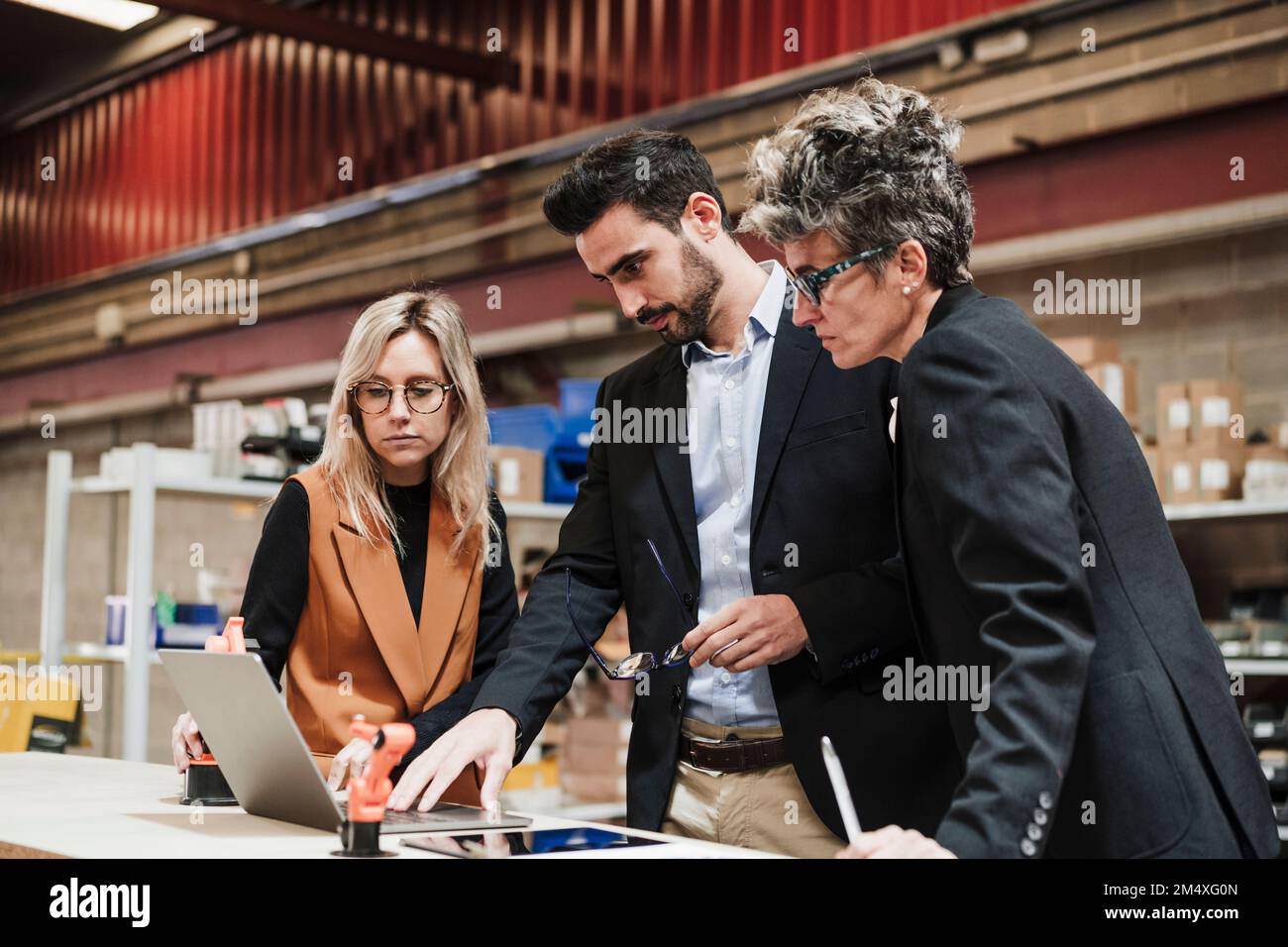 Uomo d'affari che discute con le donne d'affari sopra il laptop all'industria Foto Stock
