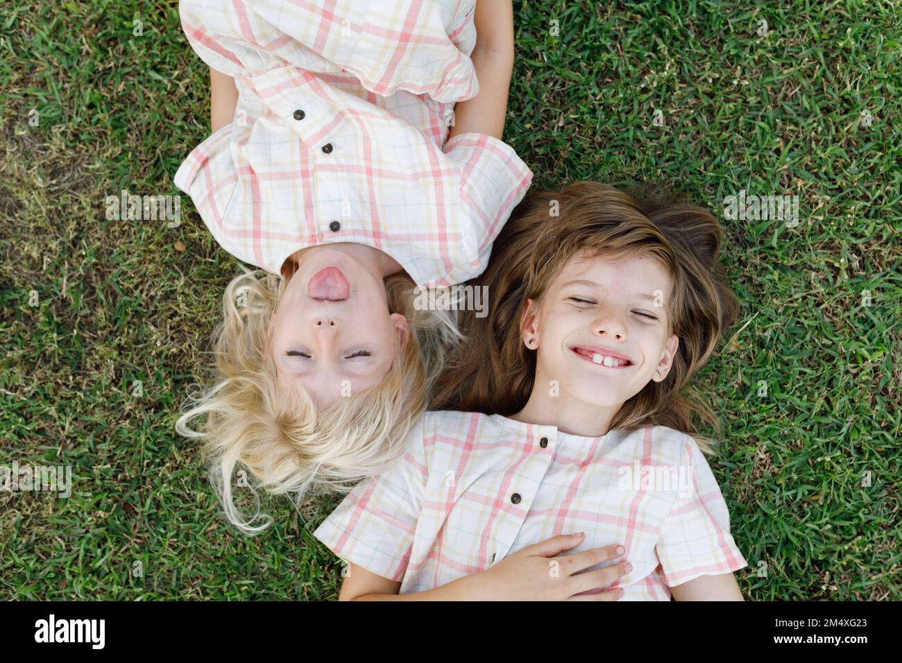 Ragazza carina che si aggetta verso l'esterno lingua sdraiata da sorella felice sull'erba Foto Stock