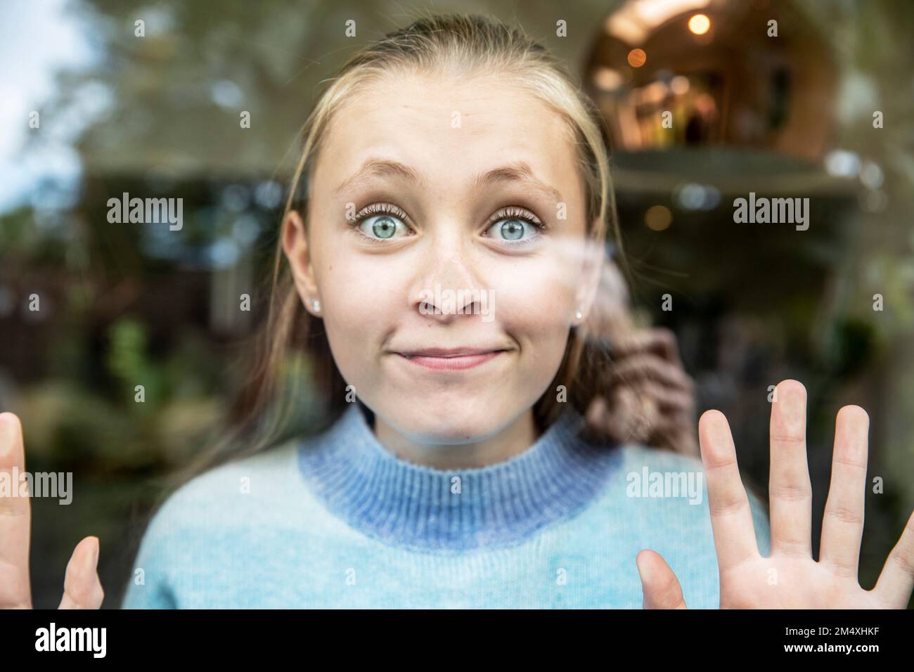 Ragazza sorridente che preme il naso sulla finestra di vetro Foto Stock