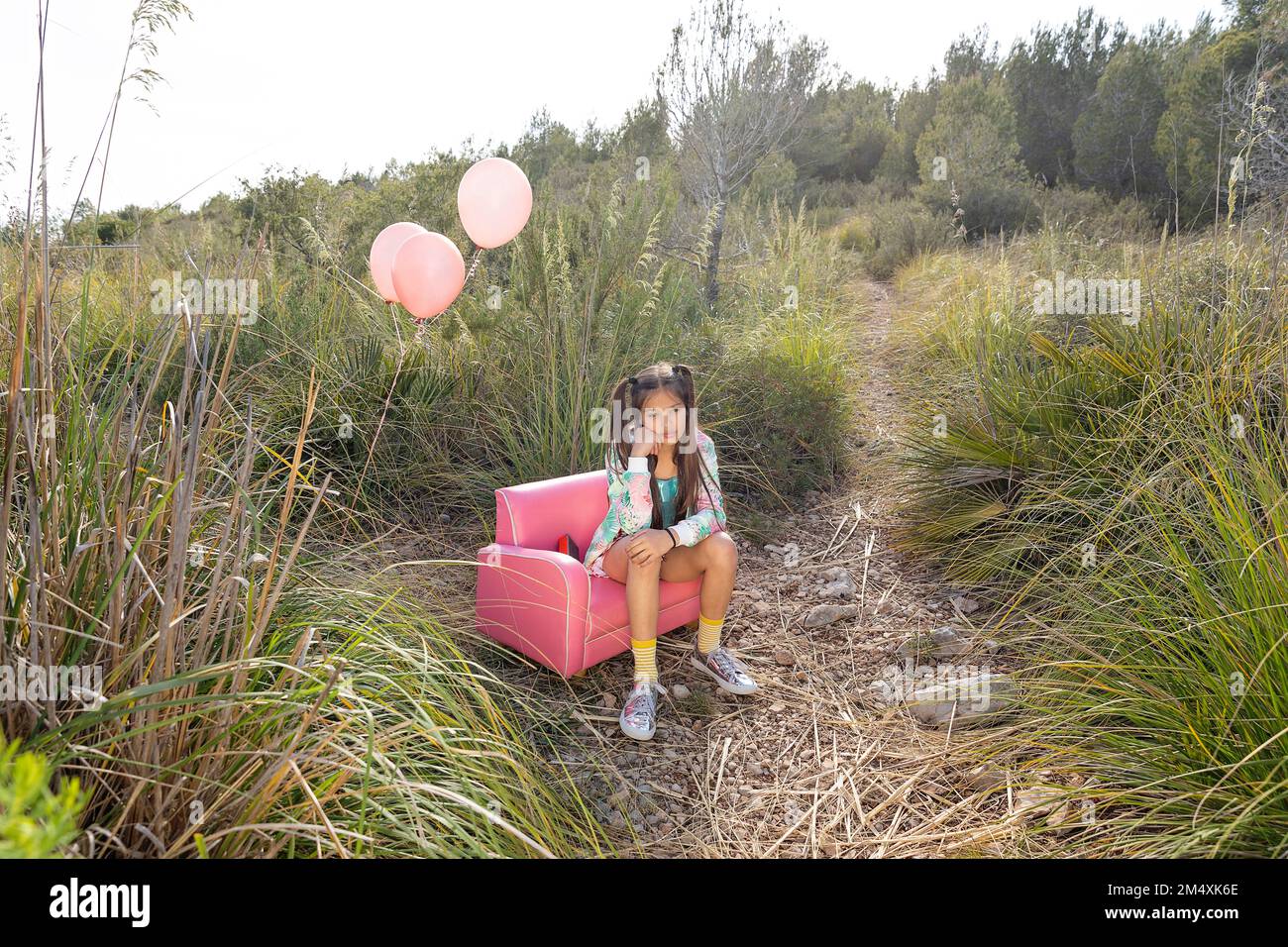Ragazza premurosa seduta su poltrona rosa in campo Foto Stock