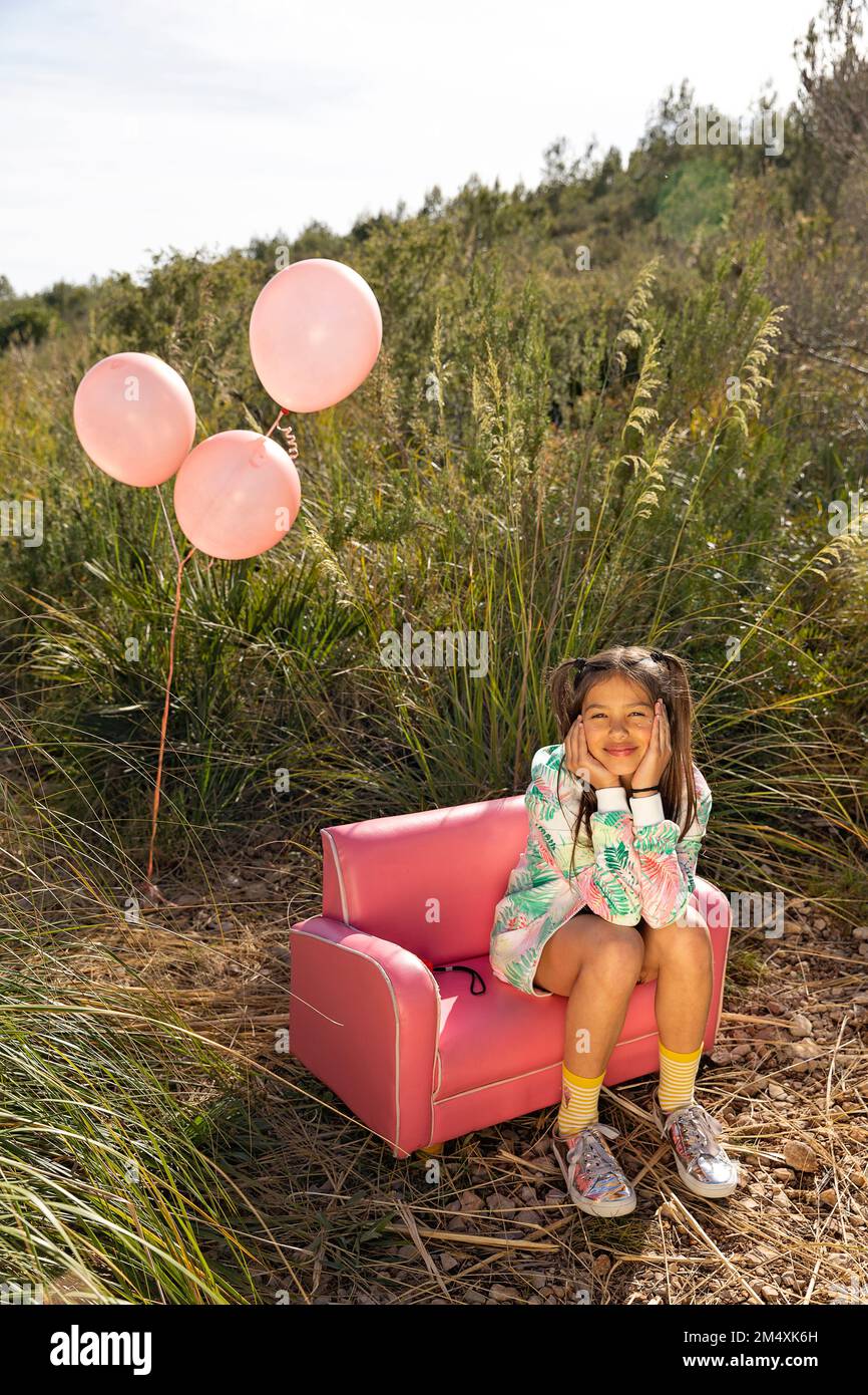 Ragazza simpatica e sorridente seduta con la testa in mano sulla poltrona rosa Foto Stock
