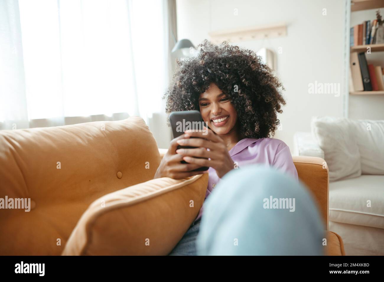 Donna sorridente che usa lo smartphone sul divano del soggiorno Foto Stock
