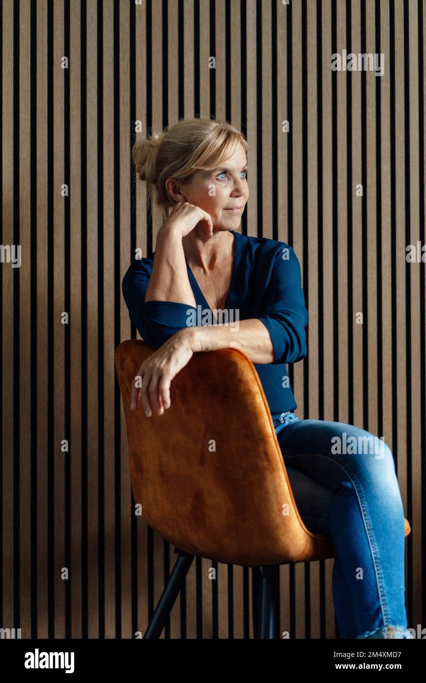 Donna d'affari premurosa seduta sulla poltrona di fronte alla parete a strisce Foto Stock