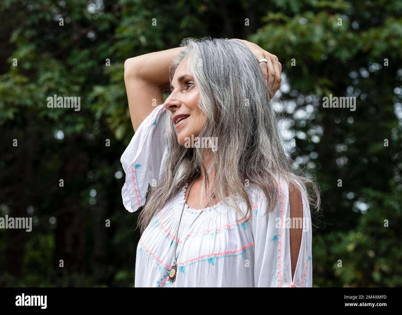 Donna sorridente dai capelli grigi con braccio sollevato nella foresta Foto Stock