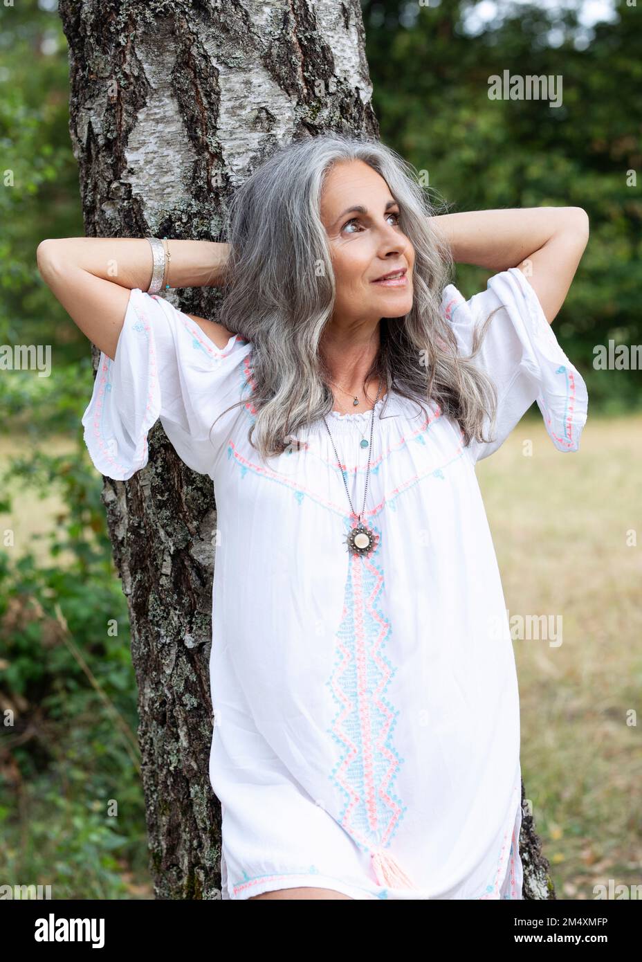 Donna premurosa con le mani dietro la testa appoggiata sul tronco dell'albero Foto Stock