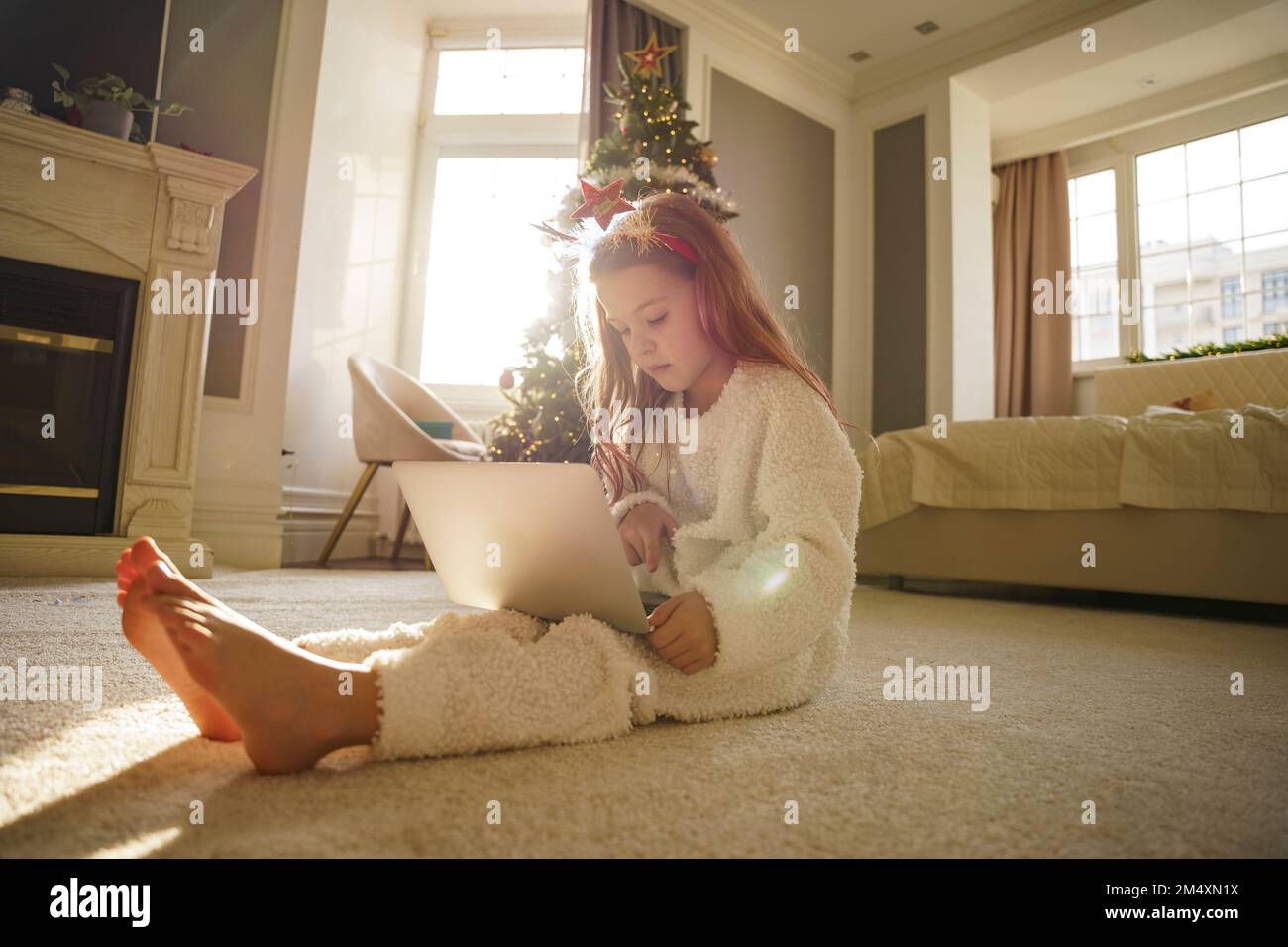 Ragazza seduta sul tappeto utilizzando il computer portatile in camera da letto a casa Foto Stock