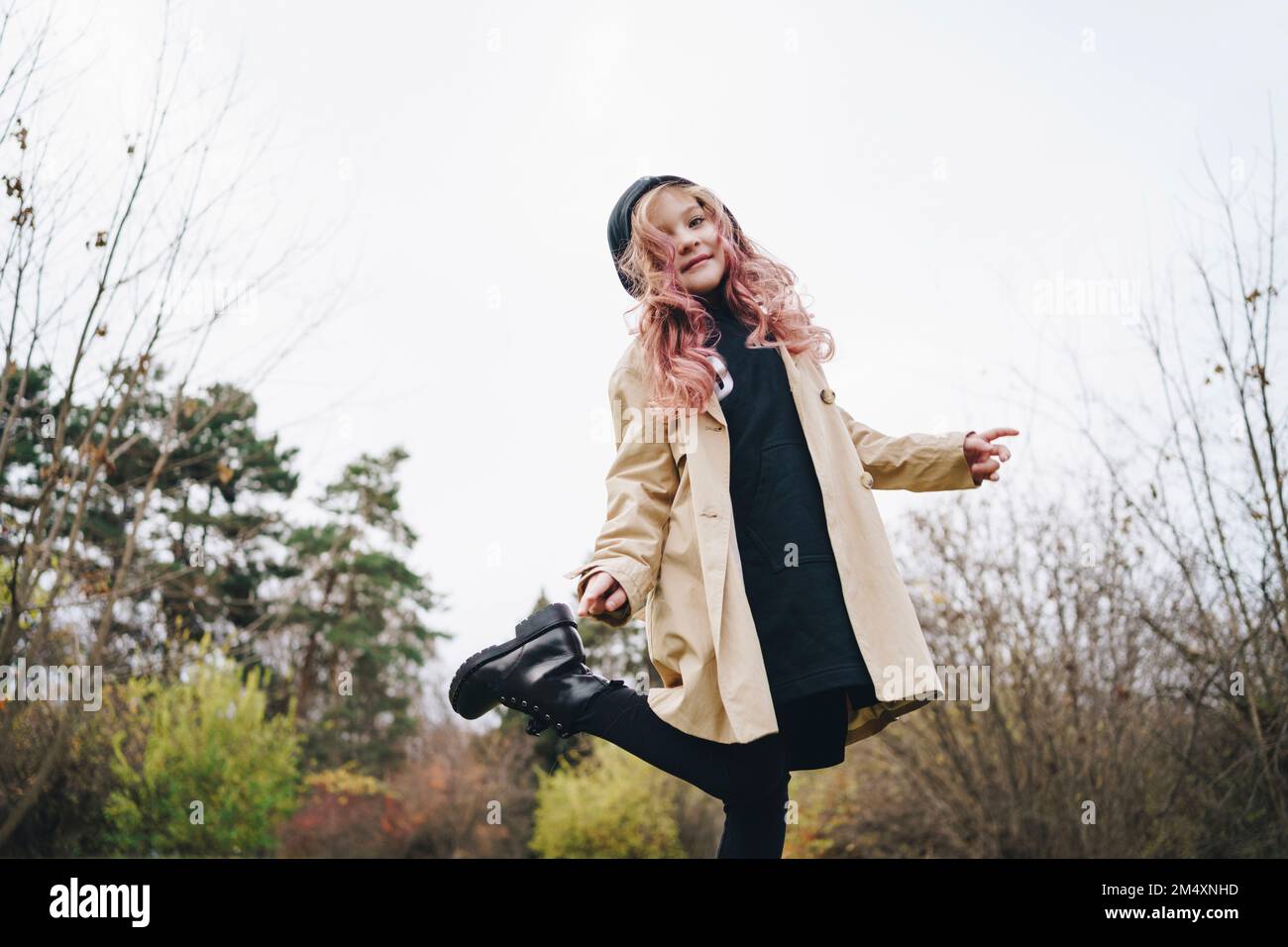Ragazza sorridente con capelli rosa in piedi nel parco sotto il cielo Foto Stock