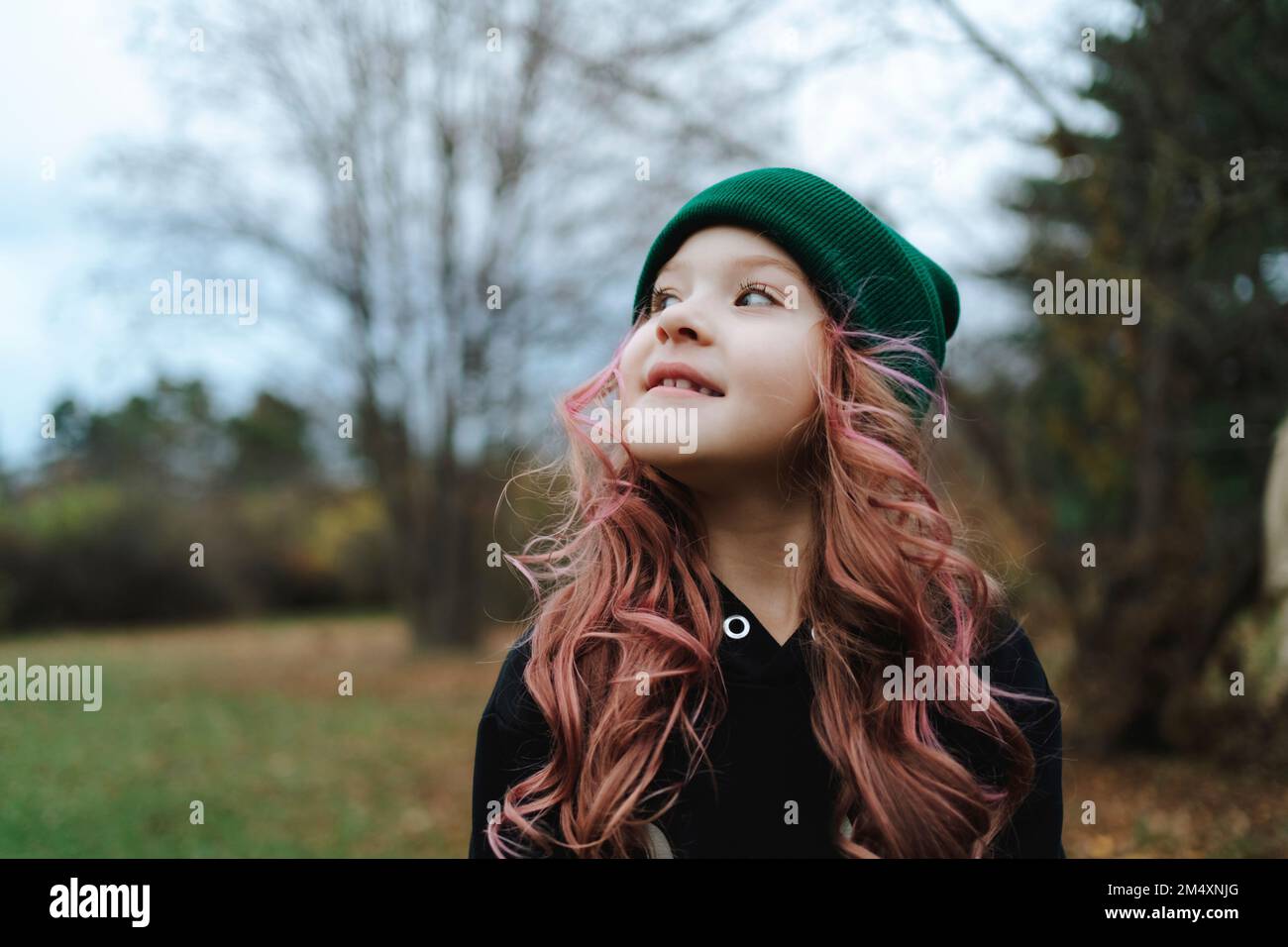 Ragazza sorridente con i capelli rosa che indossano il cappello di maglia nel parco Foto Stock