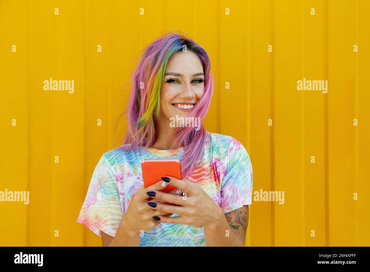 Felice giovane donna che tiene il telefono cellulare di fronte al muro giallo Foto Stock