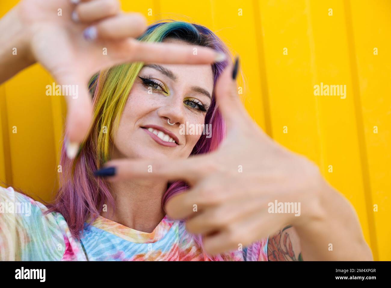 Giovane donna sorridente che fa la cornice del dito davanti al muro giallo Foto Stock