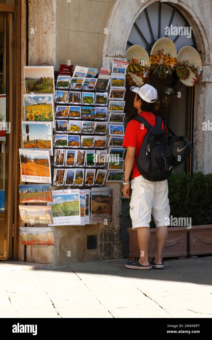 Turista studiando cartoline colorate fuori da un negozio nella città toscana di Pienza, Val d'Orcia, Toscana, Italia Foto Stock