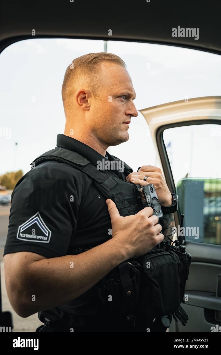 Ufficiale di polizia maschio bianco in piedi fuori dal veicolo per indagare su una situazione in una città in un pomeriggio caldo. Foto Stock