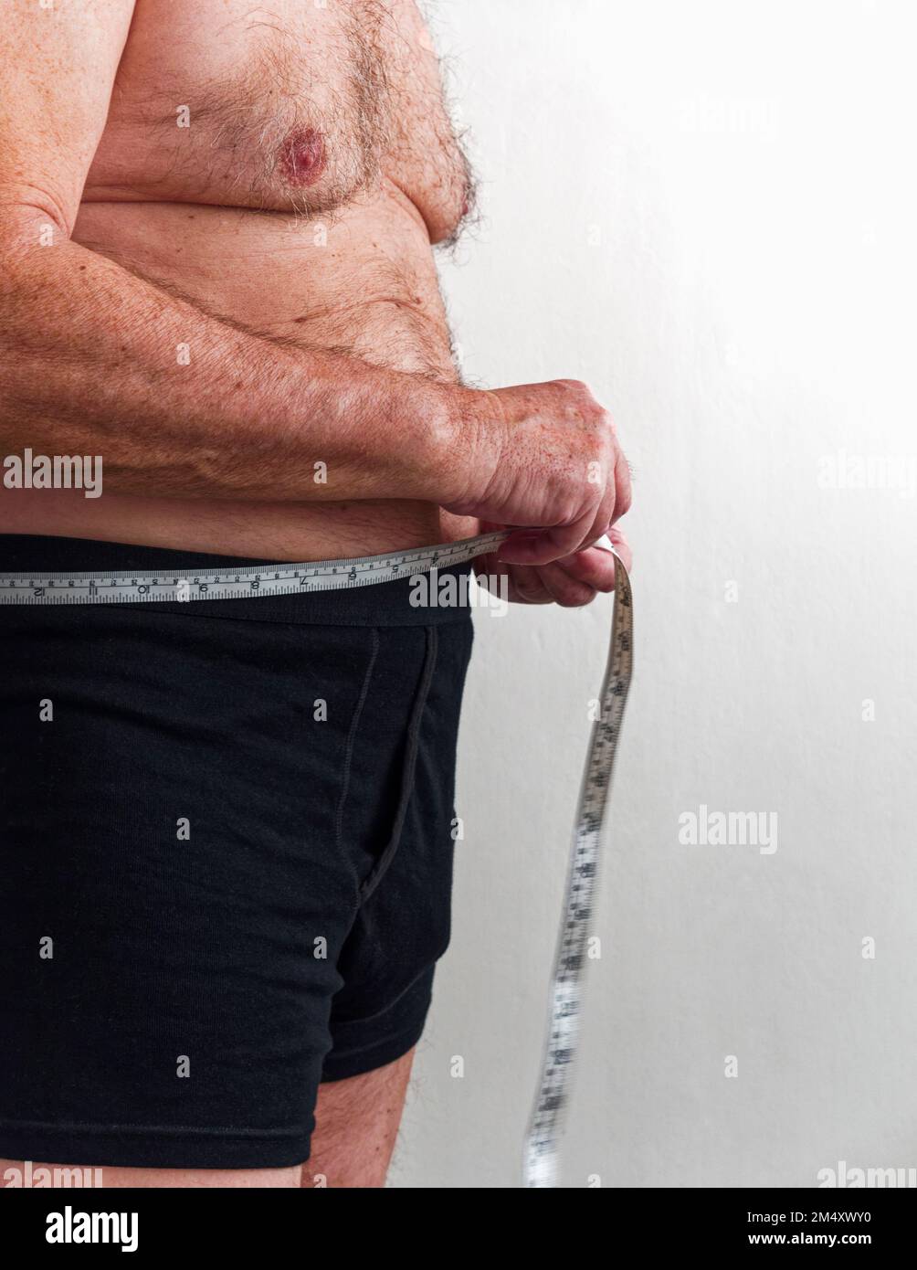 Uomo maturo in boxer Shorts misura la sua vita con un metro a nastro Foto Stock