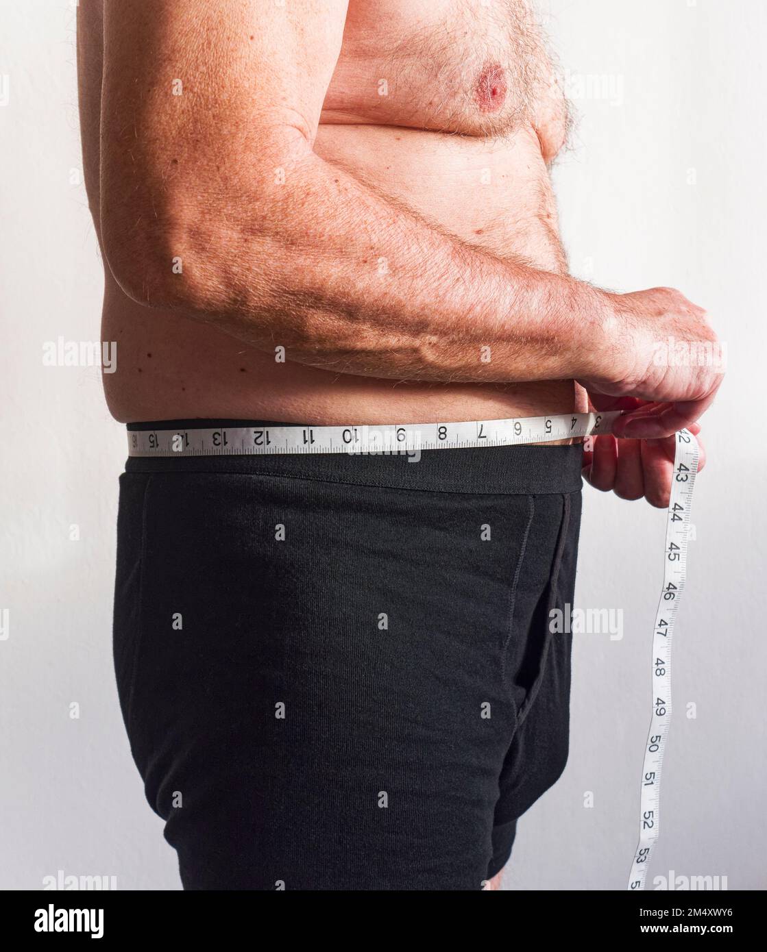 Uomo maturo in boxer Shorts misura la sua vita con un metro a nastro Foto Stock
