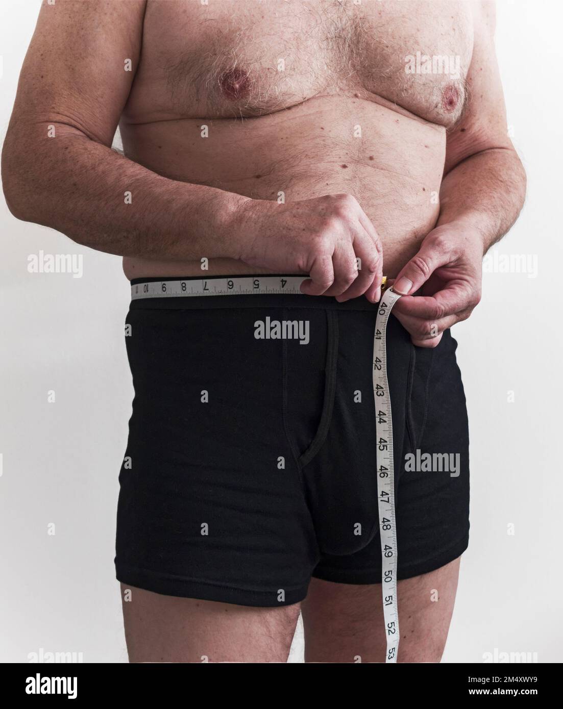 Uomo maturo in boxer Shorts misura la sua vita con un metro a nastro Foto Stock