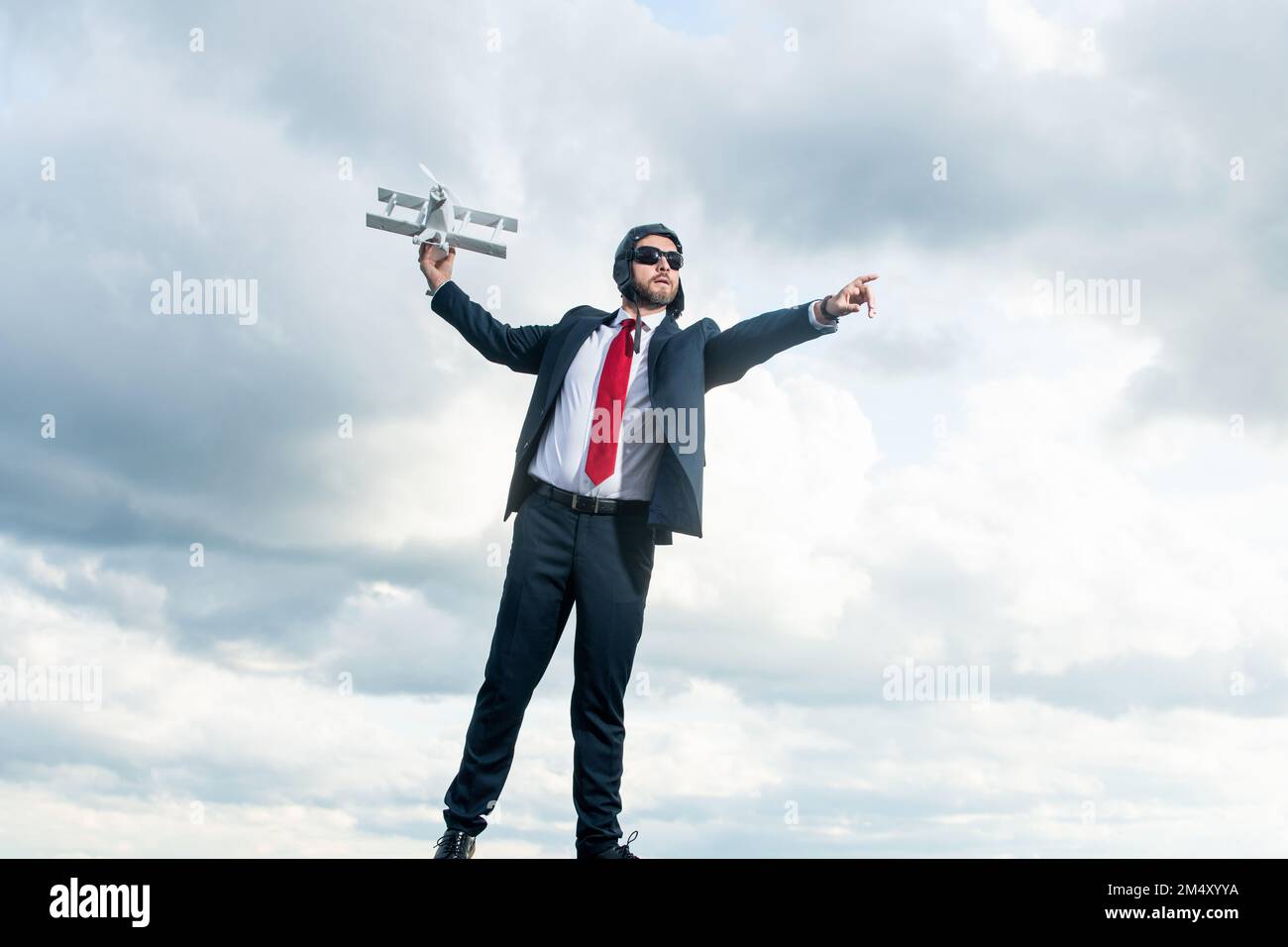 uomo d'affari in tuta e cappello pilota boost aereo giocattolo su sfondo cielo Foto Stock