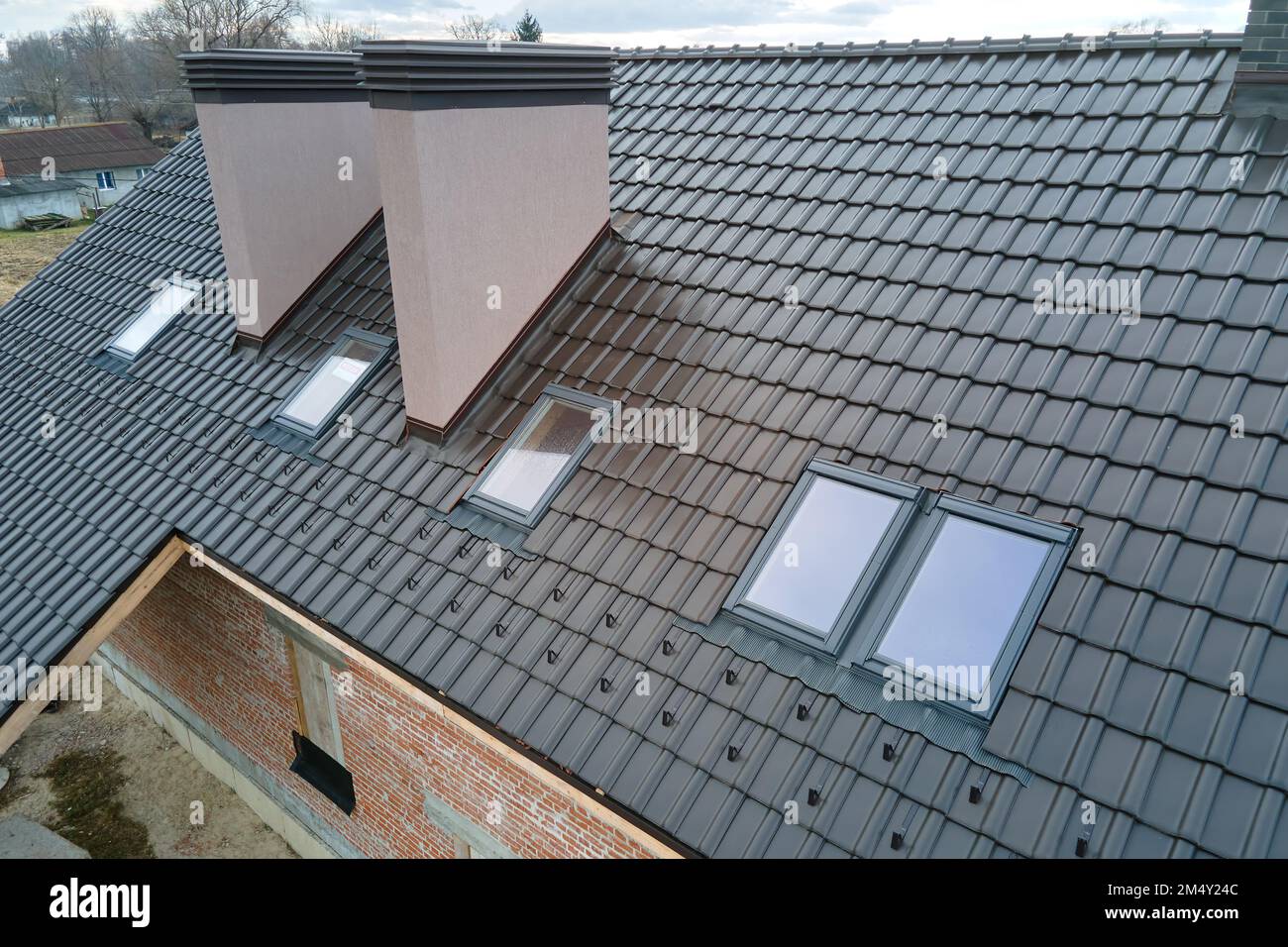 Primo piano di finestre sottotetto e camini in mattoni sul tetto della casa coperto con scandole in ceramica. Rivestimento piastrellato dell'edificio Foto Stock