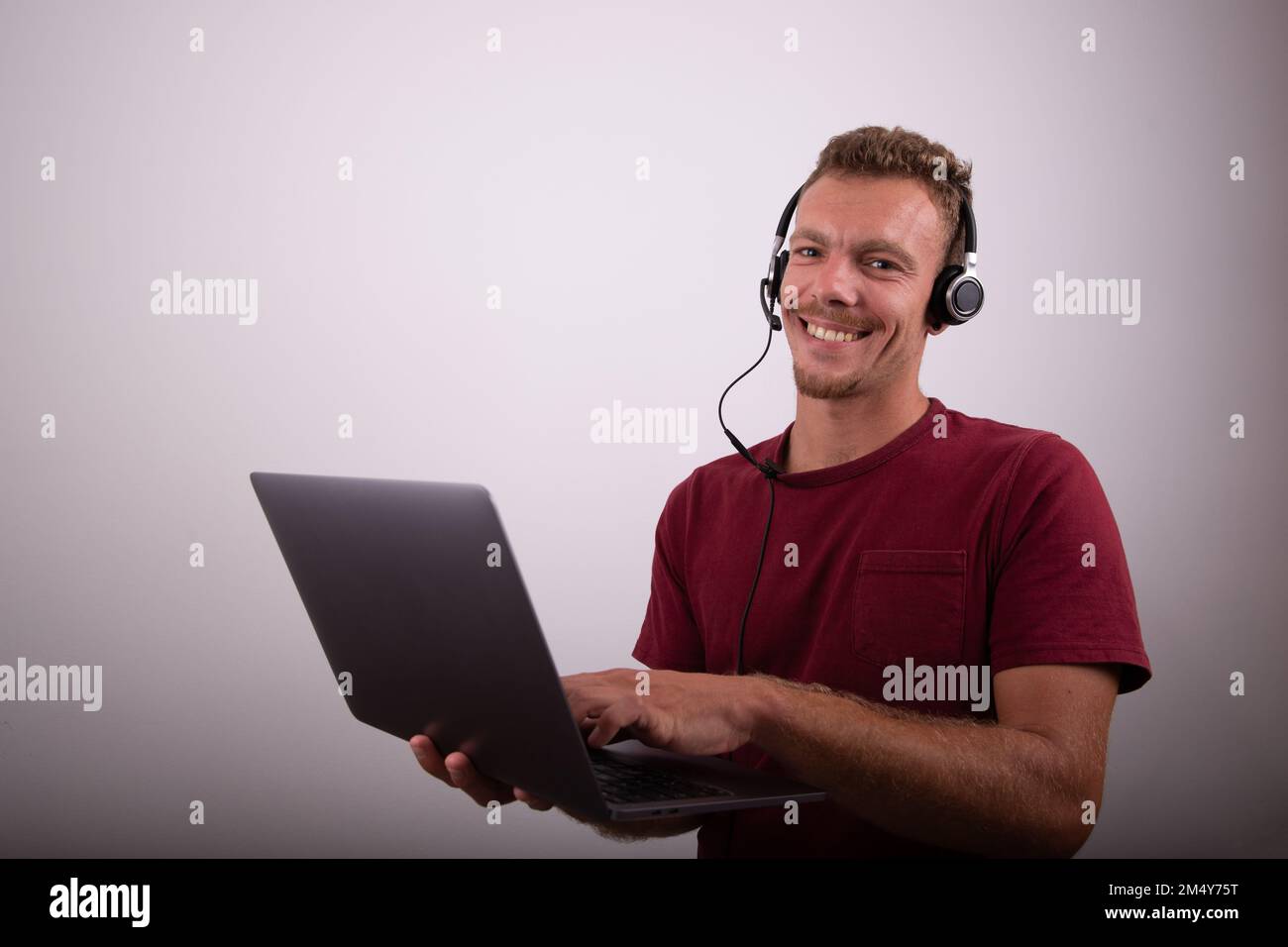 Un uomo tiene un computer portatile e indossa auricolari con microfono, call center, foto pubblicitaria in studio con spazio per la copia Foto Stock