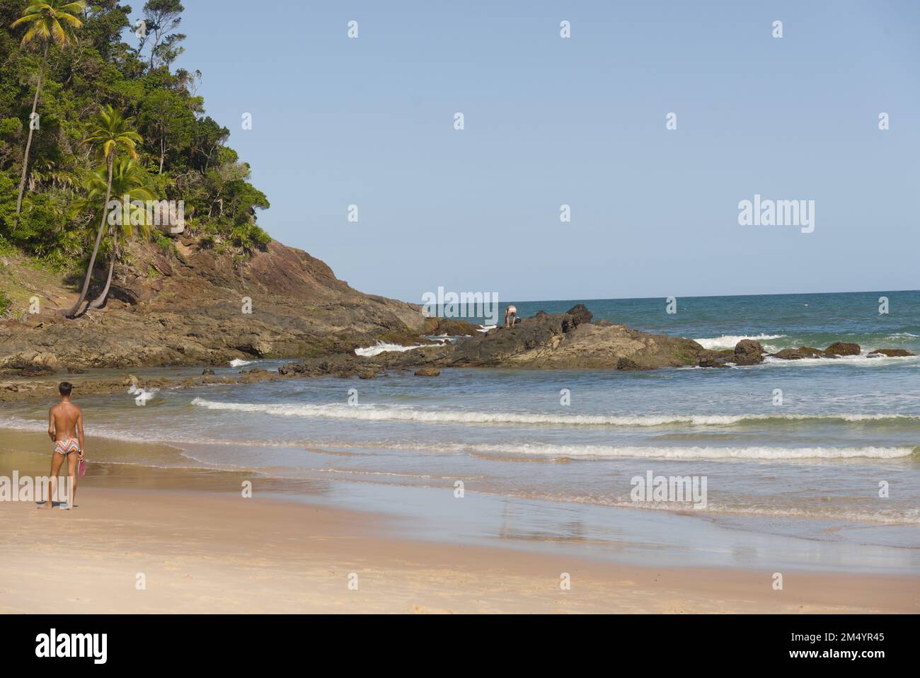 Bella vista panoramica di una spiaggia paradisiaca con rilievo roccioso in una giornata di sole con cielo blu, nuvole bianche e alcuni bagnanti Foto Stock