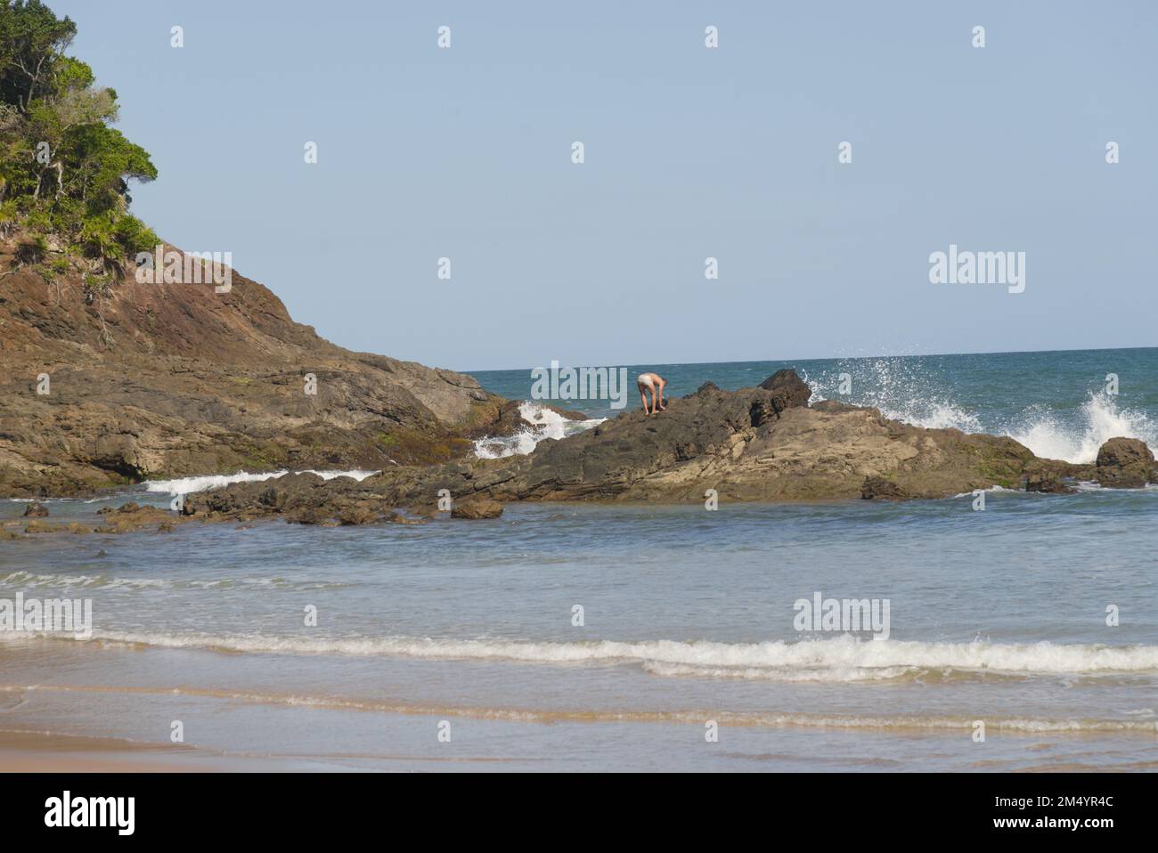 Bella vista panoramica di una spiaggia paradisiaca con rilievo roccioso in una giornata di sole con cielo blu, nuvole bianche e un sole Foto Stock