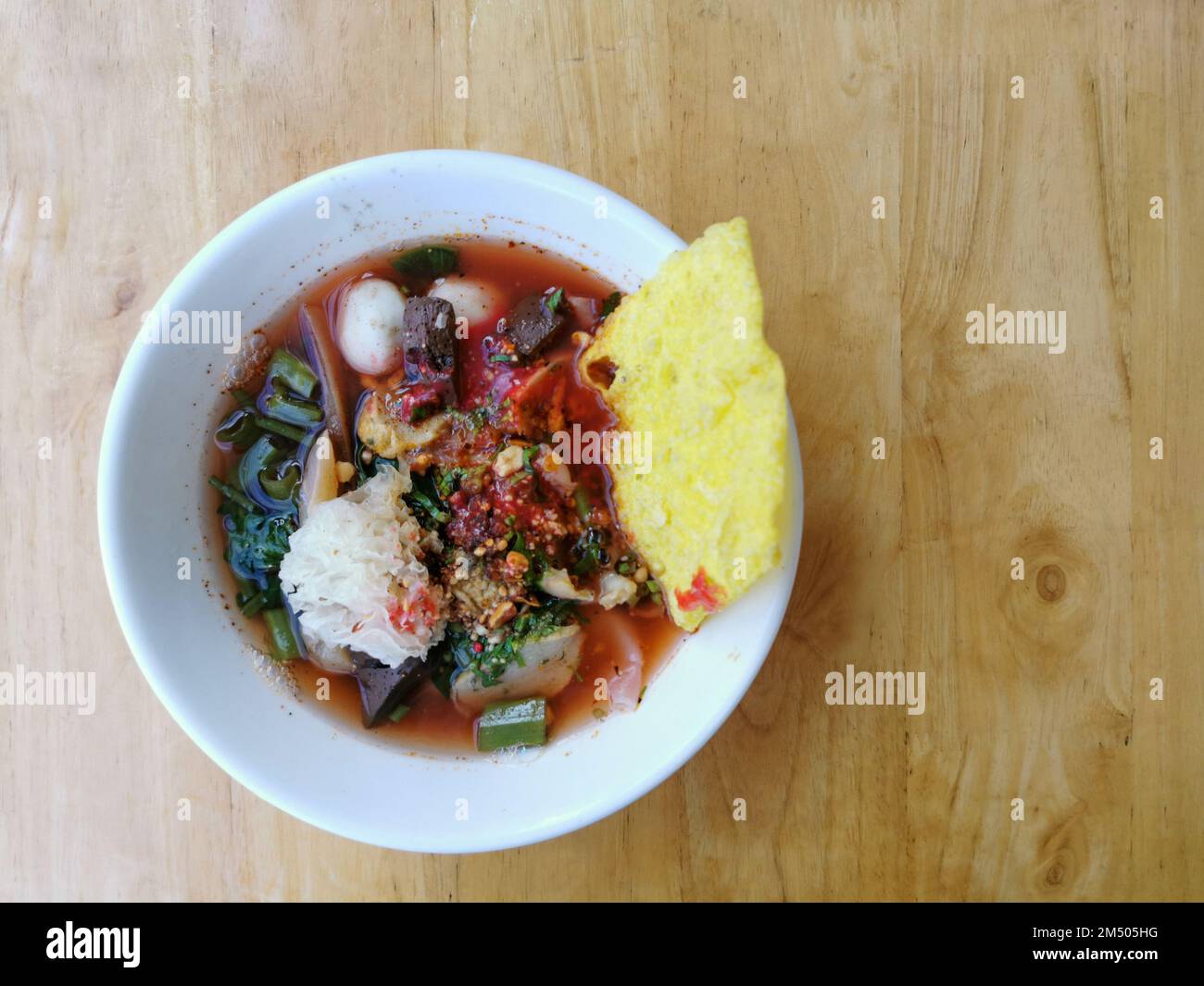 Yen ta fo o Young tao fo. Una zuppa di noodle tailandese con palla di pesce, calamari, wonton fritto e verdure in un recipiente bianco su sfondo di legno. Cibo di strada tailandese Foto Stock