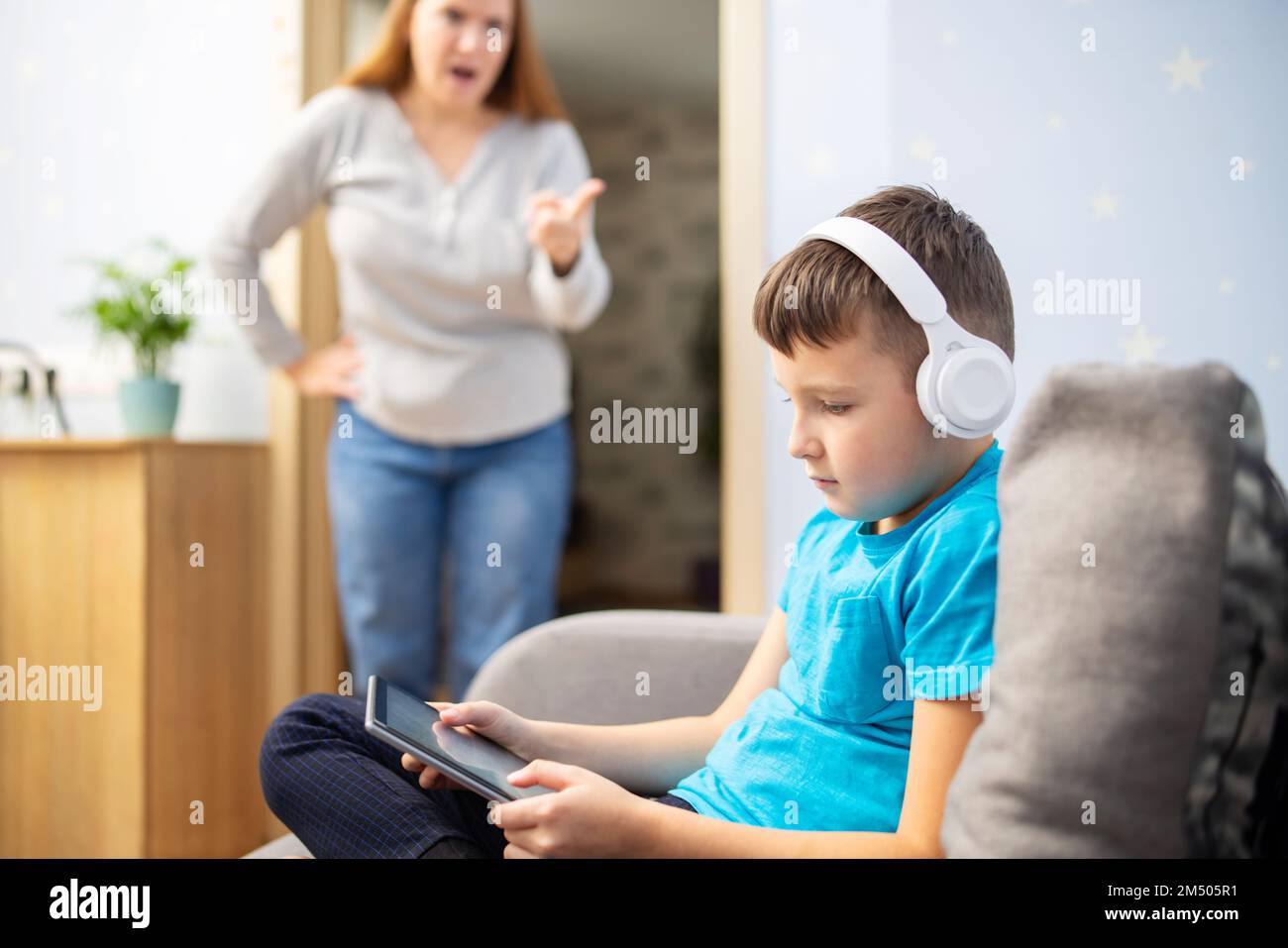 Madre scolda suo figlio. Il ragazzo usa il tablet con le cuffie e ignora la mamma Foto Stock