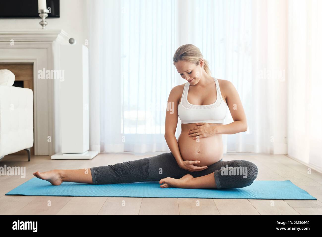 Anche le bambine saranno un fan del fitness. una donna incinta che fa yoga su un tappetino per l'esercizio fisico a casa. Foto Stock
