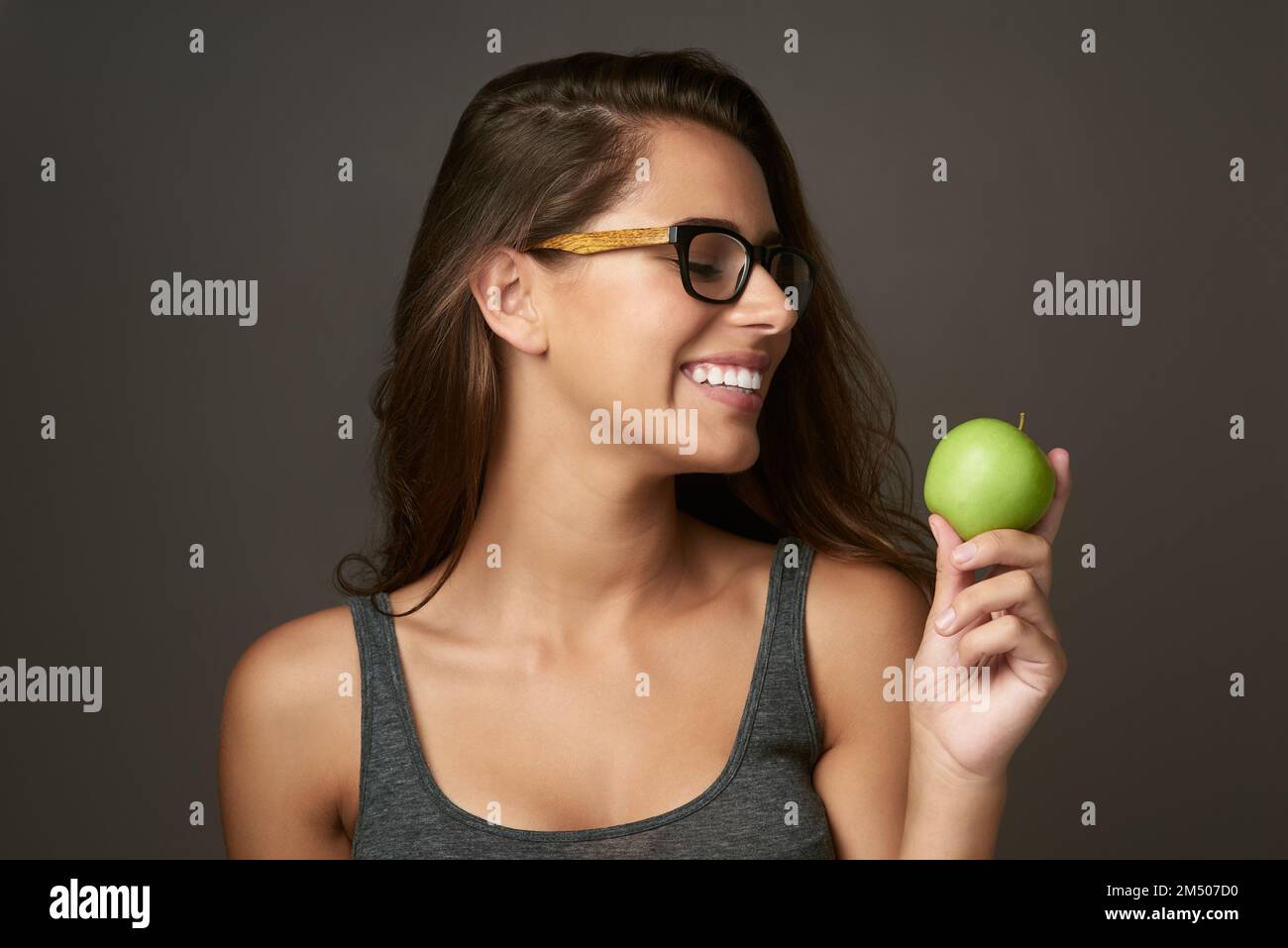Guardate voi il frutto bello. Studio shot di una bella giovane donna che guarda una mela su uno sfondo marrone. Foto Stock