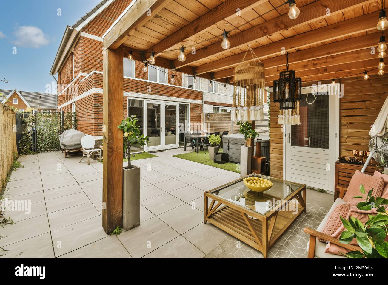 un'area soggiorno all'aperto con mobili da patio e piante in vaso sul lato della casa, circondata da pareti in mattoni Foto Stock