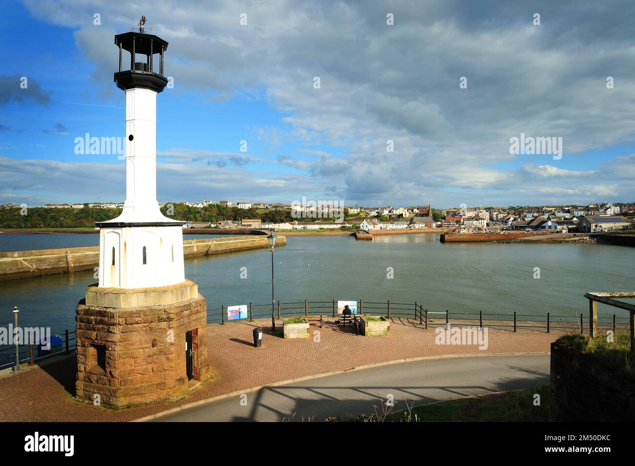 Una bella vista di un faro a Maryport, Cumbria in Inghilterra, con un porto e una vista sulla città sullo sfondo, in una giornata di sole con le nuvole Foto Stock