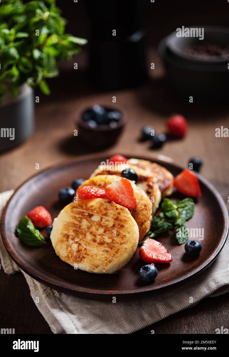 Frittelle al formaggio o sciroppi con menta, fragole e mirtilli su un tavolo di legno scuro. Concetto buio e nutriente colazione sana. Macro e Foto Stock