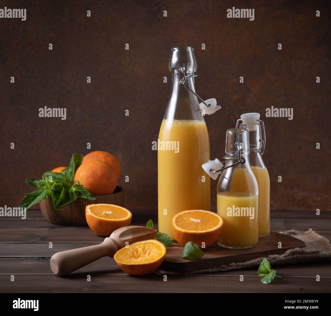 spremuta d'arancia fresca in tre bottiglie con agrumi sul tagliere e fondo di legno marrone. Concetto rustico. Immagine vista frontale Foto Stock