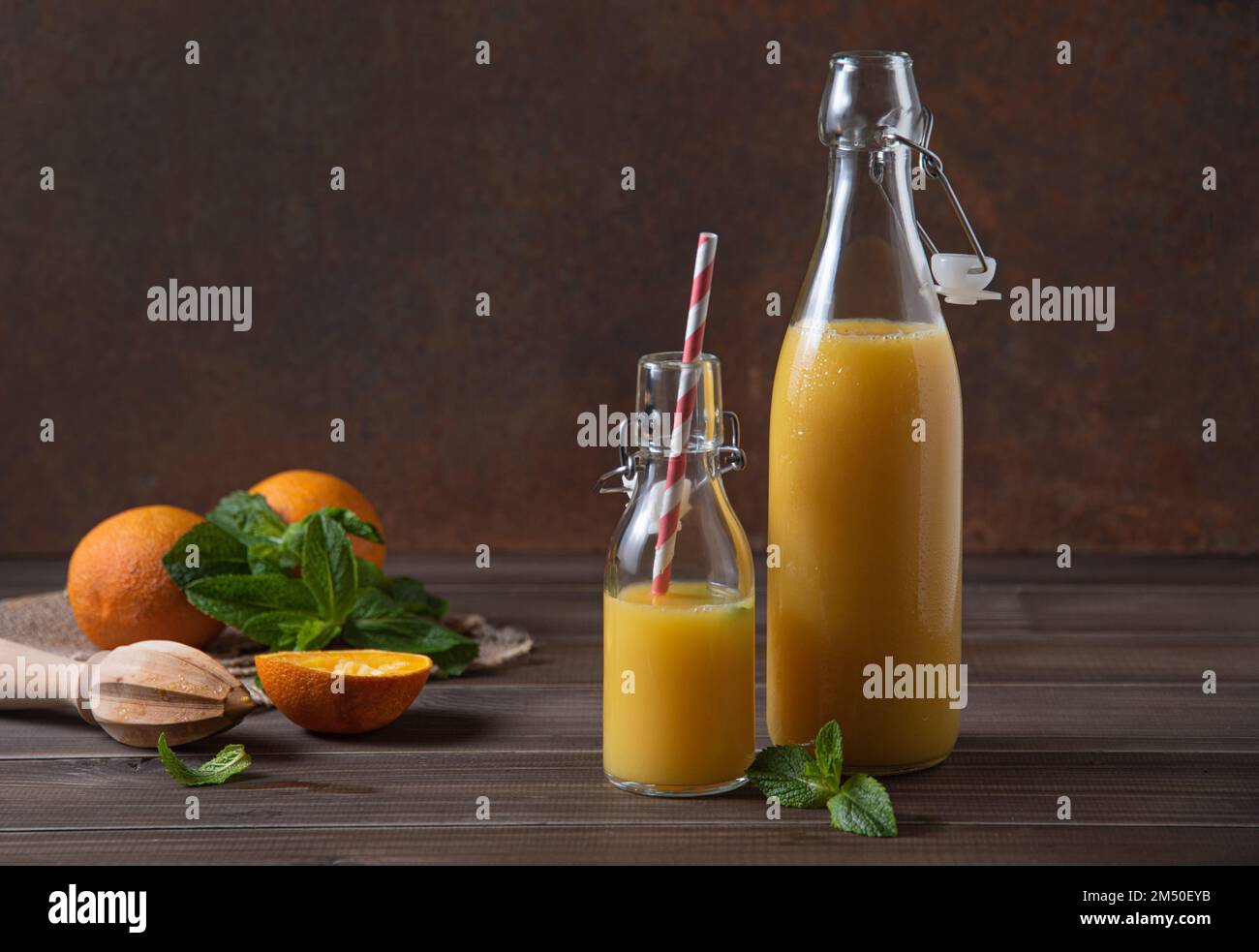 spremuta d'arancia fresca in due bottiglie con agrumi su fondo di legno marrone. Concetto rustico. Immagine vista frontale Foto Stock