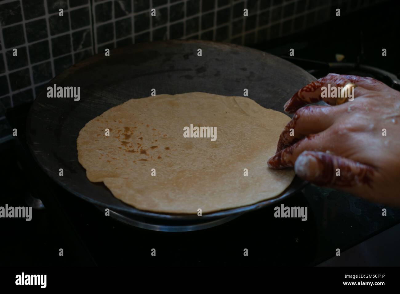 Un'immagine di un cucchiaio pieno di ghee sul pane caldo di grano indiano (chapati) in cucina. La focalizzazione principale è sul cucchiaio. Foto Stock