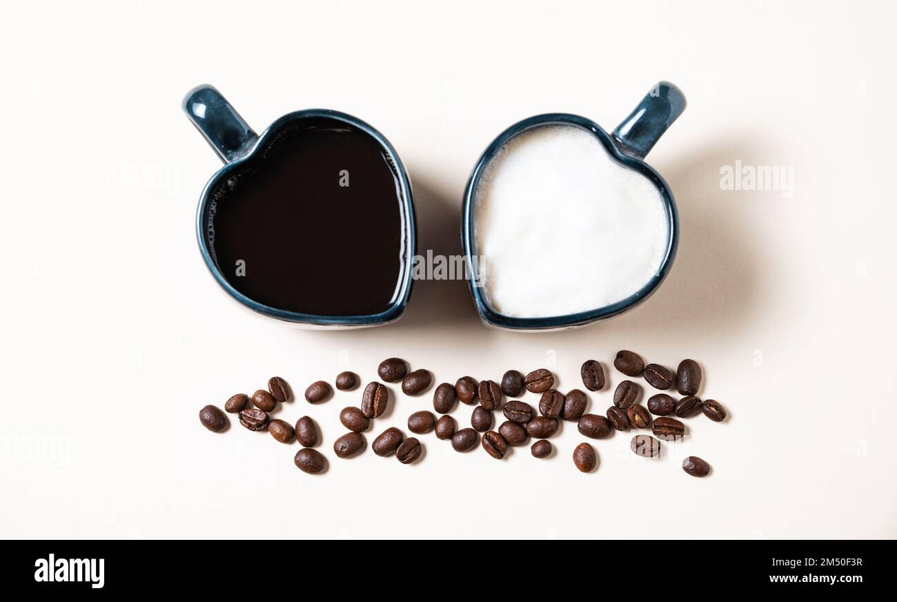 Due tazze a forma di cuori con caffè aromatico appena preparato con latte ed espresso e grani sparsi su fondo giallo. Il concetto di op Foto Stock