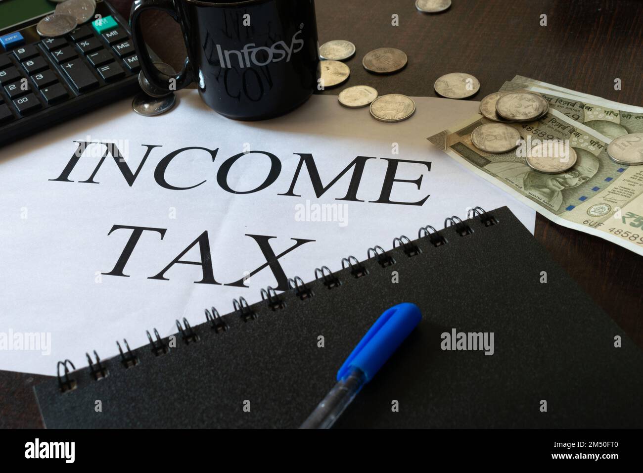 Immagine dell'imposta sul reddito scritta su una pagina con calcolatore, diario, contanti, penna e una tazza di Infosys. Bilancio, dichiarazione dei redditi, deposito, azienda, commessa, savi Foto Stock