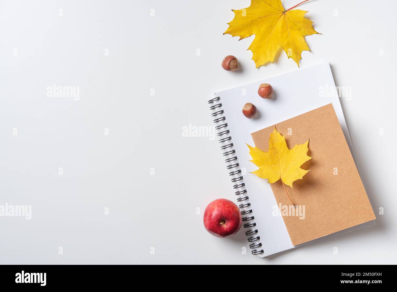 Concept autunno piatto con foglie di acero giallo su un notebook e blocco note e una mela rossa su un tavolo bianco. Vista dall'alto e spazio di copia. Foto Stock