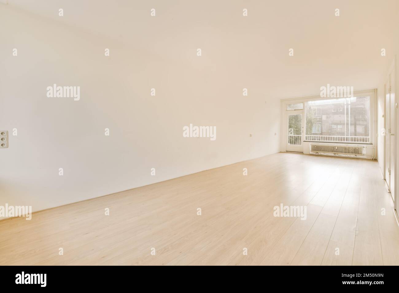 una stanza vuota con pareti bianche e pavimento in legno sulla destra, c'è una grande finestra sulla sinistra Foto Stock